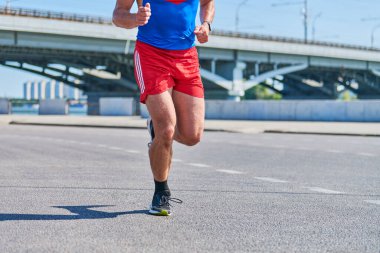 Koşan adam. Şehir yolunda spor kıyafetleriyle koşan atletik bir adam. Sağlıklı yaşam tarzı, spor hobisi. Sokak çalışması, açık hava koşusu.