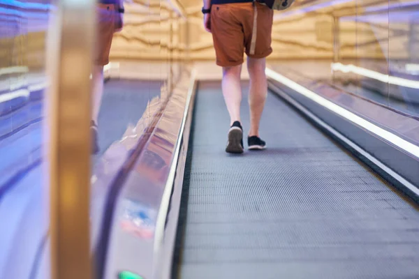 Young man goes down on moving walkway in shopping center. Horizontal slow-moving conveyor mechanism for easy elevation. Travelator for easy moving to food store.