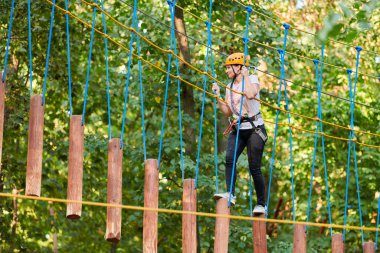 Yüksek ipli bir kız macera ağacı parkı deneyimi yaşıyor. Ağaçlardaki halat yolu parkuru. Macera halat parkına tırmanıyorum. Tahta köprü ve yüksek tel etkinliği.