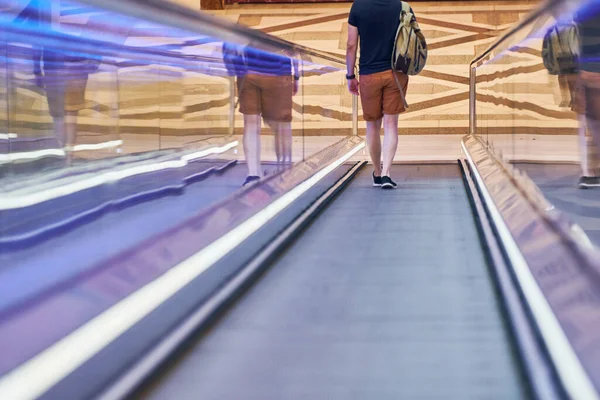 Young man goes down on moving walkway in shopping center. Horizontal slow-moving conveyor mechanism for easy elevation. Travelator for easy moving to food store.