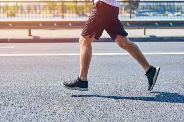 Koşan adam. Şehir yolunda spor kıyafetleriyle koşan atletik bir adam. Sağlıklı yaşam tarzı, spor hobisi. Sokak çalışması, açık hava koşusu.