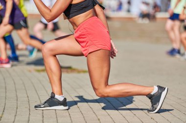 Genç bir kadın maraton koşmadan önce ısınıyor. Bronz bacaklı güzel bir kız. Açık hava fitness germe egzersizi. Spor partisi.