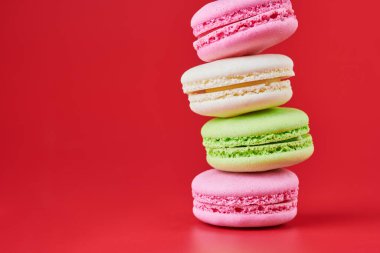 Kırmızı arka planda makaronlar. Badem ve hindistan cevizinden renkli küçük kurabiyeler. Popüler şekerlemeler. Atıştırmalık lezzetli yemekler, kopyalama alanı