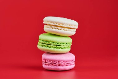 Kırmızı arka planda makaronlar. Badem ve hindistan cevizinden renkli küçük kurabiyeler. Popüler şekerlemeler. Atıştırmalık lezzetli yemekler, kopyalama alanı