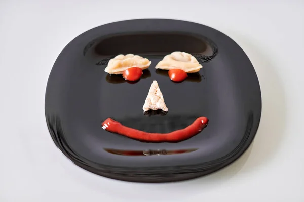 Funny food face, dumpling and ketchup. Food art on black plate. Smiling face on plate. Motivation for losing weight and healthy eating.