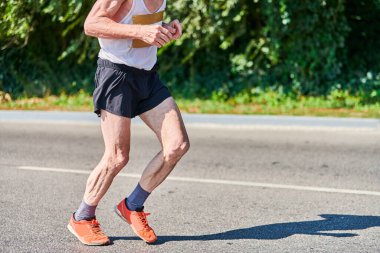 Koşan yaşlı adam. Şehir yolunda spor kıyafetleriyle koşan yaşlı bir adam. Sağlıklı yaşam tarzı, spor hobisi. Sokak çalışması, açık hava koşusu.