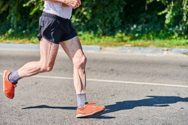 Koşan yaşlı adam. Şehir yolunda spor kıyafetleriyle koşan yaşlı bir adam. Sağlıklı yaşam tarzı, spor hobisi. Sokak çalışması, açık hava koşusu.