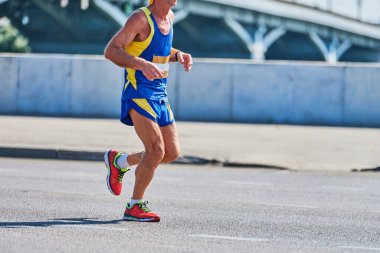 Koşan yaşlı adam. Şehir yolunda spor kıyafetleriyle koşan yaşlı bir adam. Sağlıklı yaşam tarzı, spor hobisi. Sokak çalışması, açık hava koşusu.