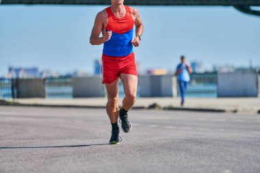 Koşan adam. Şehir yolunda spor kıyafetleriyle koşan atletik bir adam. Sağlıklı yaşam tarzı, spor hobisi. Sokak çalışması, açık hava koşusu.