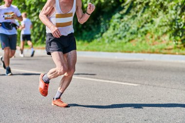 Koşan yaşlı adam. Şehir yolunda spor kıyafetleriyle koşan yaşlı bir adam. Sağlıklı yaşam tarzı, spor hobisi. Sokak çalışması, açık hava koşusu.