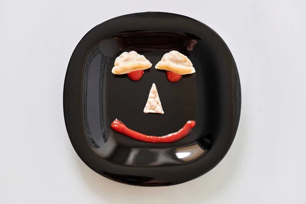 Food face, funny dumpling and ketchup. Smiling face on plate. Food art on black plate. Motivation for losing weight and healthy eating.