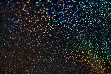 Gökkuşağı pırıltısı. Soyut zemin. Renkli parlayan gökkuşağı damlaları ve siyah arka planda ışıklar. Bulanık pulların ve bokeh 'in şenlikli parlak parıltısı..