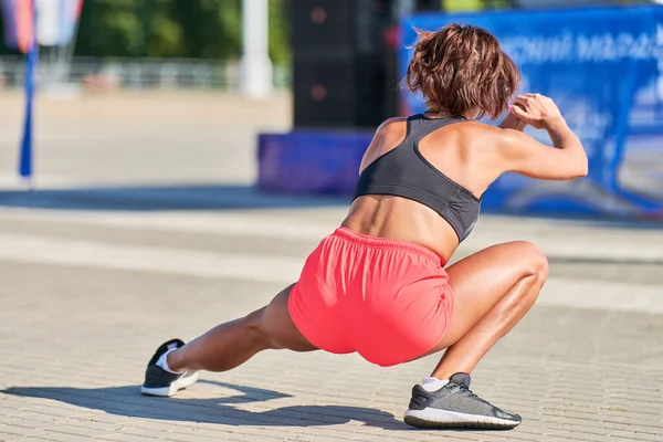 Genç bir kadın maraton koşmadan önce ısınıyor. Bronz bacaklı güzel bir kız. Açık hava fitness germe egzersizi. Spor partisi.