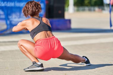 Genç bir kadın maraton koşmadan önce ısınıyor. Bronz bacaklı güzel bir kız. Açık hava fitness germe egzersizi. Spor partisi.