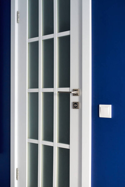 Белая внутренняя дверь с ручкой. Голубая стена в современной квартире, выключатель света рядом. Wooden закрытая дверь между комнатами. Стильный дизайн коридоров