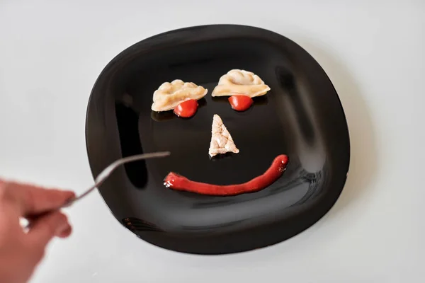 Food face, funny dumpling and ketchup. Smiling face on plate. Food art on black plate. Motivation for losing weight and healthy eating.