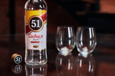 Moskova - 23.11.2019 - Cachaca 51 şişesi ve iki bardak. Brezilya romu. Egzotik Brezilya alkolü mayalanmış şeker kamışı suyu. Çatı katı daire arka planı.