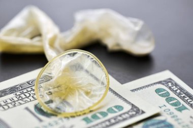 Used condom with cum and US dollars bills. Prostitution concept. Pay for sex per night. Harlotry and whoredom. US dollar money on table with contraceptive.