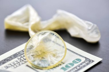 Used condom and US dollars bills. Cum in condom. Prostitution concept. Pay for sex per night. Harlotry and whoredom. US dollar money on table with contraceptive.