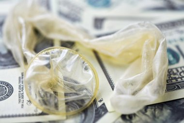 Used condom with cum and US dollars bills. Prostitution concept. Pay for sex per night. Harlotry and whoredom. US dollar money on table with contraceptive.