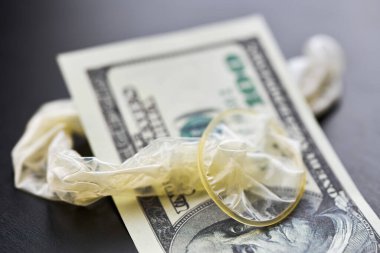 Used condom and US dollars bills. Cum in condom. Prostitution concept. Pay for sex per night. Harlotry and whoredom. US dollar money on table with contraceptive.