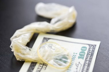 Used condom with cum and US dollars bills. Prostitution concept. Pay for sex per night. Harlotry and whoredom. US dollar money on table with contraceptive.