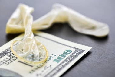 Used condom with cum and US dollars bills. Prostitution concept. Pay for sex per night. Harlotry and whoredom. US dollar money on table with contraceptive.