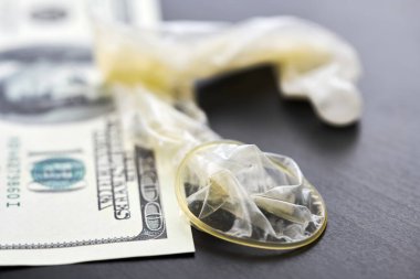 Used condom with cum and US dollars bills. Prostitution concept. Pay for sex per night. Harlotry and whoredom. US dollar money on table with contraceptive.