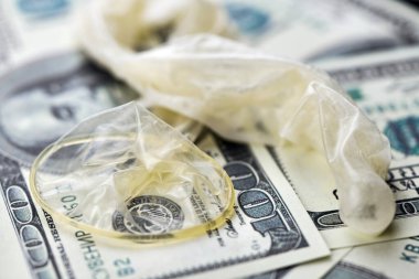 Used condom with cum and US dollars bills. Prostitution concept. Pay for sex per night. Harlotry and whoredom. US dollar money on table with contraceptive.