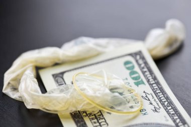 Used condom with cum and US dollars bills. Prostitution concept. Pay for sex per night. Harlotry and whoredom. US dollar money on table with contraceptive.
