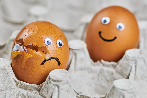 Смешное яйцо и грустное разбитое яйцо в подносе для яиц. Два пасхальных куриных яйца, свежие и натуральные. Концепция доставки, пространство для копирования.