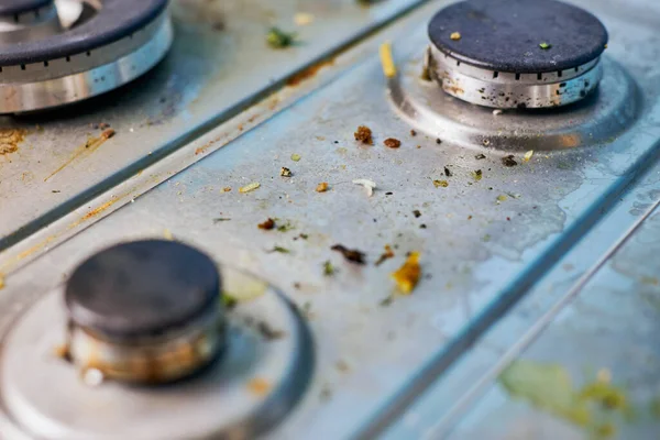 Dirty gas stove top with food leftovers. Unclean steel kitchen cooktop with greasy spots. Spring-cleaning, remove kitchen old fat stains, fry spots, oil splatters and burned-on bits