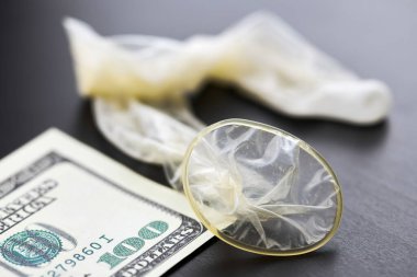 Used condom with cum and US dollars bills. Prostitution concept. Pay for sex per night. Harlotry and whoredom. US dollar money on table with contraceptive.