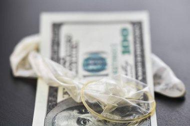 Used condom with cum and US dollars bills. Prostitution concept. Pay for sex per night. Harlotry and whoredom. US dollar money on table with contraceptive.