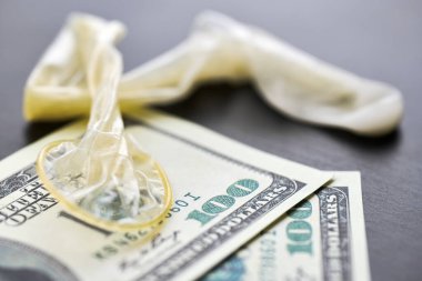 Used condom and US dollars bills. Cum in condom. Prostitution concept. Pay for sex per night. Harlotry and whoredom. US dollar money on table with contraceptive.