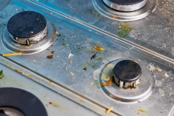 Dirty gas stove top with food leftovers. Unclean steel kitchen cooktop with greasy spots. Spring-cleaning, remove kitchen old fat stains, fry spots, oil splatters and burned-on bits