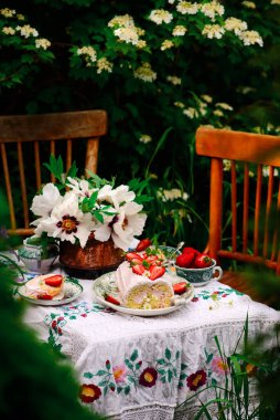 Sünger rulo çilek ve kremayla yaz bahçesindeki bir sette klasik bir odak noktası.