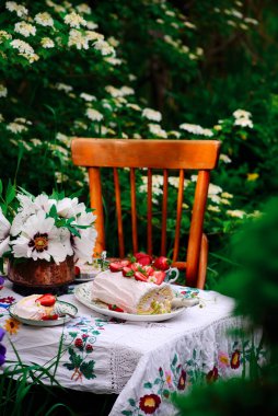 Sünger rulo çilek ve kremayla yaz bahçesindeki bir sette klasik bir odak noktası.