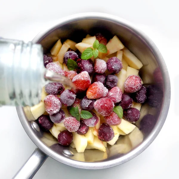 Frozen berries, cherries, strawberries and apples in a metal ladle on a white background. The process of making hot wine, mulled wine, grog, stuffing for strudel, culinary stages.