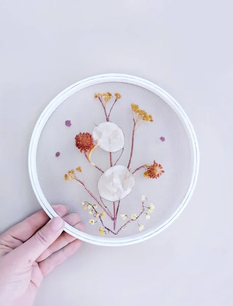 Handmade Embroidery with Dried Flowers and withered herbs on mesh fabric, grid, tulle, round hoop on background. Home Decor, interior, walls. Step-by-step masterclass, handicraft guide, top view