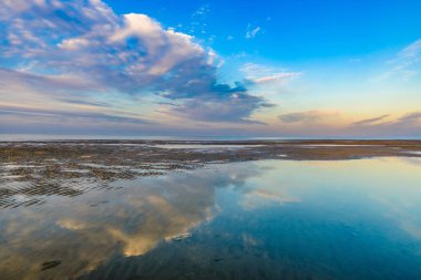 Deniz kıyısında günbatımı. Bulutlar su güzel yansıması.
