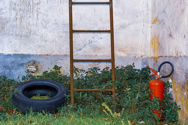 rusty ladder,old tire and fire extinguisher abandoned in an outside corner of an old house