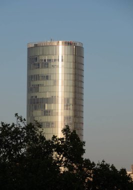 Köln, Almanya. 23 Ağustos 2023. Resmi olarak LVR Kulesi olarak bilinen Sütun Üçgeni binası, öğleden sonra geç saatlerde açık mavi gökyüzüne karşı, ön planda bazı ağaçlar ile.