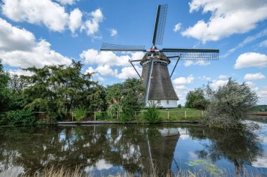 Hollanda Yeldeğirmeni su ve bulutlu mavi gökyüzü yansıtıyordu. Eski hala işleyen polder yel değirmeni, Eyaleti Güney-Hollanda, Hollanda Rotterdam'da yakın