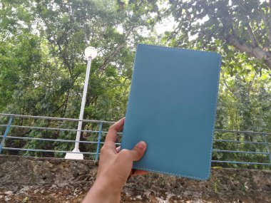 Parkta erkek el ele tutuşan defterin yakın çekimi. 