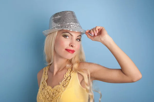 Blond meisje met glanzend zilver hoed tegen blauwe achtergrond. — Stockfoto