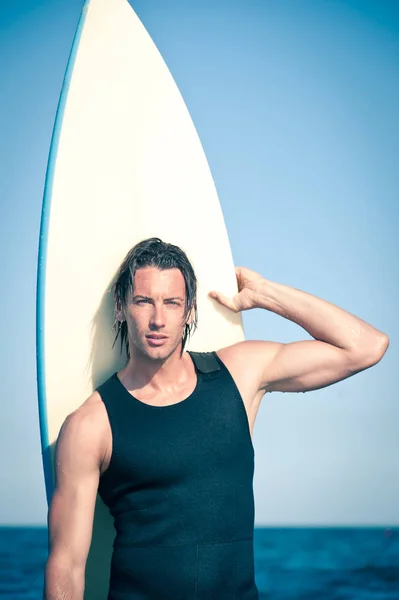 Портрет сильного молодого серфингиста на пляже с доской для серфинга — стоковое фото