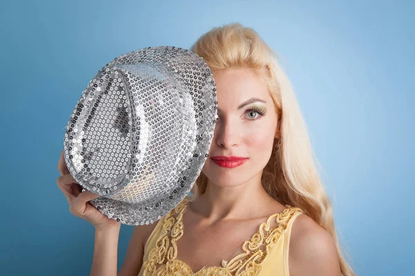 Blonde girl with shiny silver hat against blue background. — Stock Photo, Image