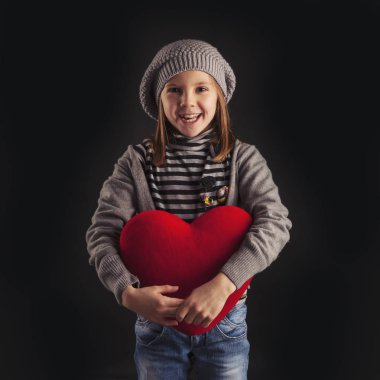 Young girl with red heart on black background. 