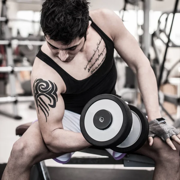 Jovem se exercitando com halteres em um ginásio. Imagem filtrada . — Fotografia de Stock